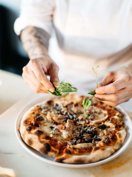 Image of someone adding toppings to a pizza